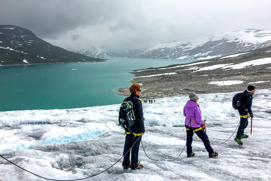 A group of hikers on Austdalsbreen overlooking Styggevatnet as dark clouds roll in during a Norway glacier hiking tour.